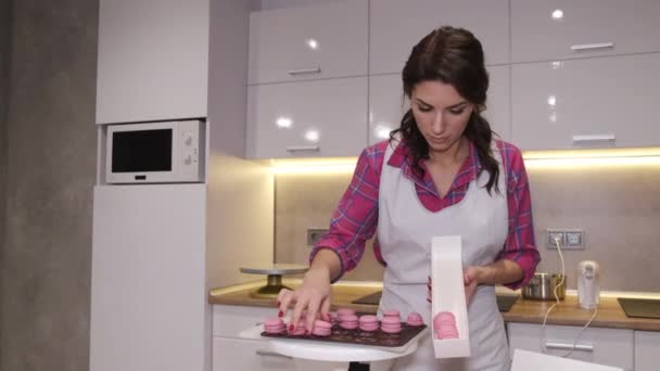 Mujer panadera bonita está poniendo macarrones horneados en una caja — Vídeo de stock