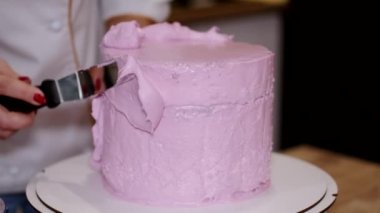 Kadın bir fırıncı pastaya pembe krema sürüyor.