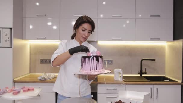 Vrouw bakker is het versieren van een verjaardagstaart met macarons aan de bovenkant — Stockvideo