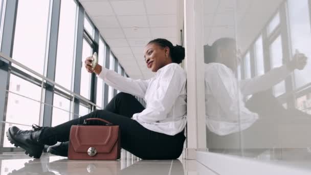 Молодая афроамериканка делает селфи в современном зале — стоковое видео