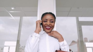 Afro-Amerikalı kadın telefonda konuşuyor ve havaalanında gülümsüyor.