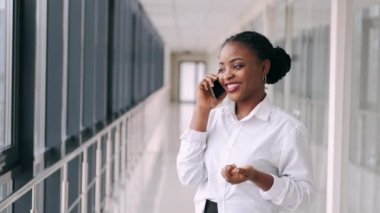 Afro-Amerikalı kadın telefonda konuşuyor ve havaalanında gülümsüyor.