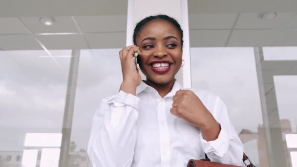 Афроамериканська жінка розмовляє по телефону і посміхається в аеропорту. — стокове відео