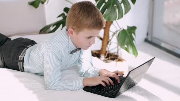 Een schooljongen typt op een laptop toetsenbord liggend op een vloer — Stockvideo