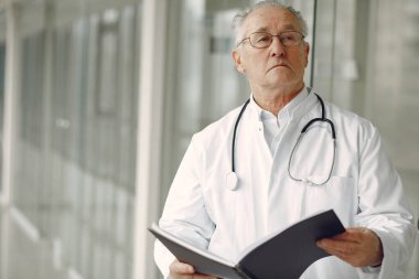 Üniformalı yaşlı doktor salonda dikiliyor.