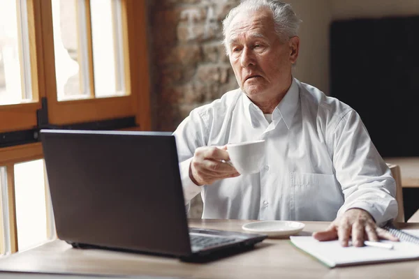 Viejo sentado a la mesa y trabajando con un portátil — Foto de Stock