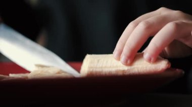 Küçük kız modern bir mutfakta muz soyuyor ve kesiyor.