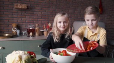 İki çocuk modern mutfakta taze salata pişiriyor.