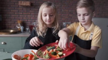 İki çocuk modern mutfakta taze salata pişiriyor.