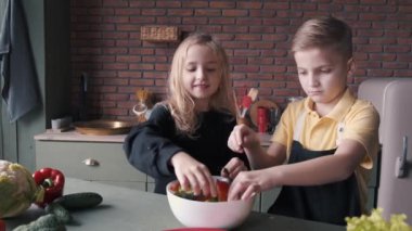 İki çocuk modern mutfakta taze salata pişiriyor.