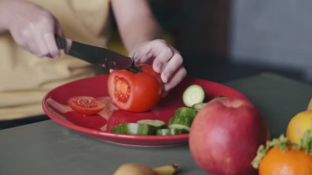 Το αγοράκι κόβει μια ντομάτα για μια σαλάτα στην κουζίνα. — Αρχείο Βίντεο