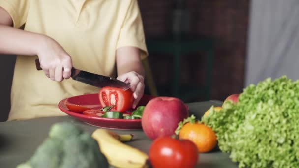 De kleine jongen snijdt een tomaat voor een salade in een keuken — Stockvideo