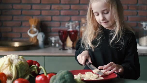 La niña está pelando y cortando un plátano en una cocina moderna — Vídeo de stock