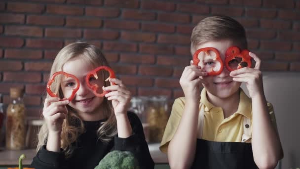 Two kids with slices of sweet pepper are in a modern kitchen having fun — Stock Video