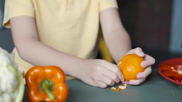 Pojken skalar en apelsin med händerna. — Stockvideo