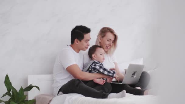 Família feliz com uma criança está relaxando na cama com um laptop — Vídeo de Stock