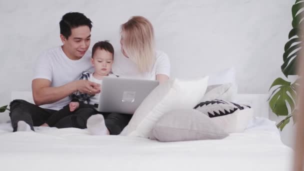 Família feliz com uma criança está relaxando na cama com um laptop — Vídeo de Stock