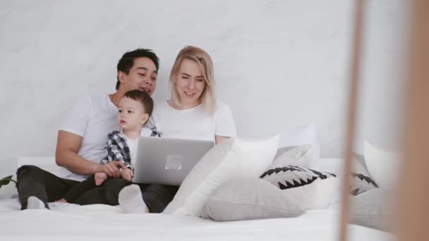 Gelukkig gezin met een kind is ontspannen op bed met een laptop — Stockvideo