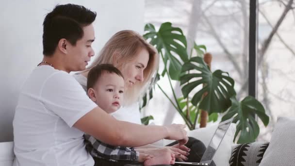 Gelukkig gezin met een kind is ontspannen op bed met een laptop — Stockvideo