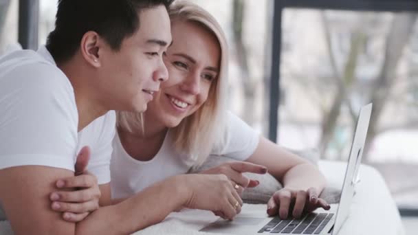 Uomo e donna si rilassano sul letto con un computer portatile — Video Stock