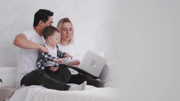 Familia feliz con un niño es relajarse en la cama con un ordenador portátil — Vídeos de Stock