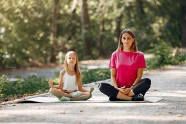Anne ve kızı yaz parkında yoga yapıyor.
