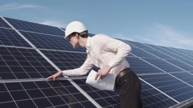 Bir adam fabrikadaki güneş enerjisi panelini kontrol ediyor.