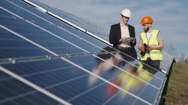 İşadamı ve işçi dışarıda güneş pillerini birlikte kontrol ediyorlar.