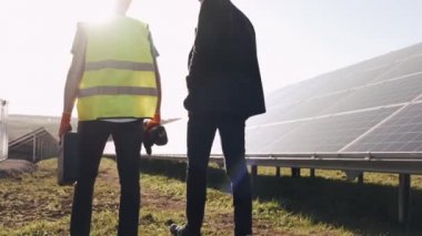 Bir işadamı ve bir işçi güneş enerjisi istasyonunda yürüyorlar.