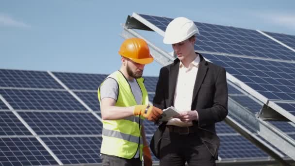 Engenheiro e um trabalhador estão discutindo algo perto de baterias solares — Vídeo de Stock