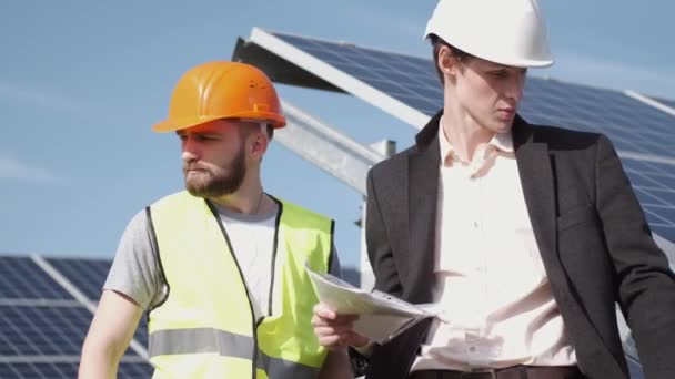 Инженер и рабочий обсуждают что-то около солнечных батарей — стоковое видео