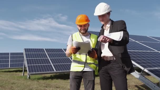 The businessman and worker are discussing documents standing near solar batteries outside — Stock Video