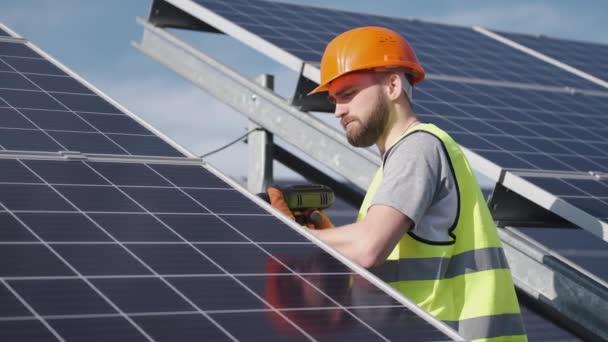 Man ingenieur in uniform controleert de zonne-energie batterij buiten — Stockvideo
