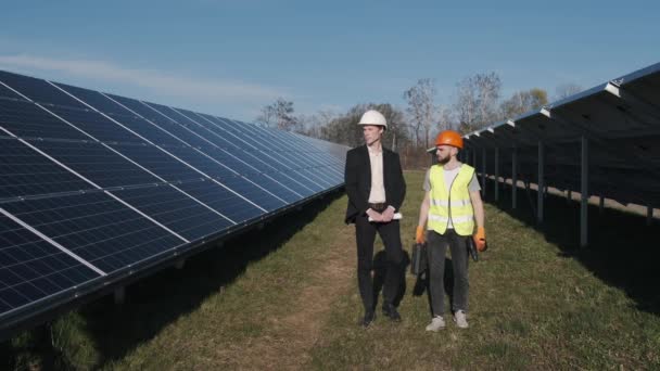 Bir işadamı ve bir işçi güneş enerjisi istasyonunda yürüyorlar. — Stok video