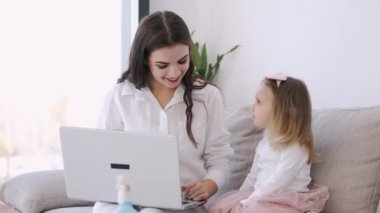 Anne ve küçük kızı bir dizüstü bilgisayarla çalışıyorlar.