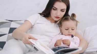 Güzel anne ve küçük kızı yatakta sarılıp kitap okuyorlar.