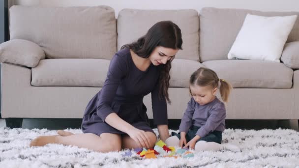 Hermosa madre y su hija pequeña están jugando juguetes de construcción juntos en una habitación — Vídeo de stock