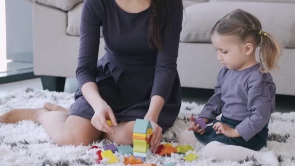 美しい母親と幼児の娘は一緒に部屋で建設おもちゃを遊んでいます — ストック動画