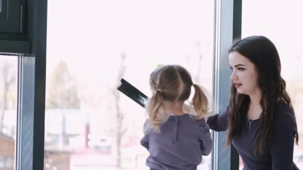 La niña está limpiando las ventanas con una fregona con su madre. — Vídeo de stock