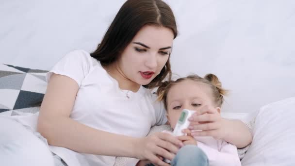 Madre está revisando la temperatura de sus hijas acostadas en la cama — Vídeo de stock