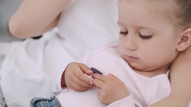 Schöne Mutter und kleine Tochter liegen im Bett und umarmen sich und lesen ein Buch — Stockvideo