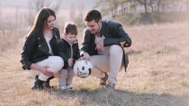 Счастливые родители и милый сын играют в футбол на улице — стоковое видео