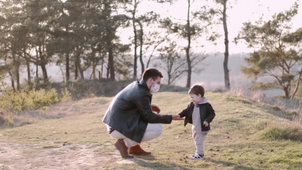 Schöner Mann mit Einwegmaske geht mit seinem Sohn draußen spazieren — Stockvideo