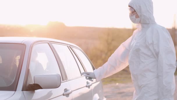 Женщина в полностью покрывающем оборудовании растягивает антибактериальную жидкость на дверной ручке автомобиля — стоковое видео