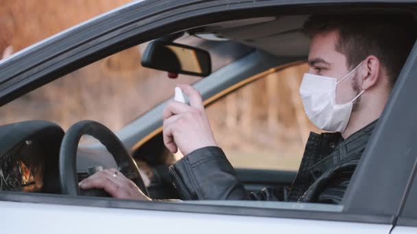 Man i en engångsmask sprutar antiseptisk på bilarna styrning — Stockvideo