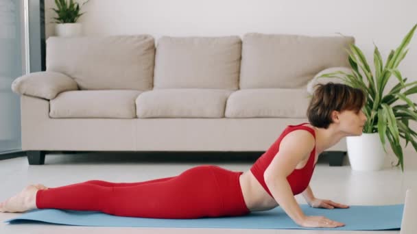 Mulher em um traje de fitness está fazendo exercícios de ioga matinal em um tapete — Vídeo de Stock