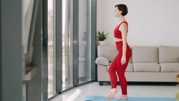 Donna in costume fitness sta facendo esercizio di yoga mattutino su un tappeto — Video Stock