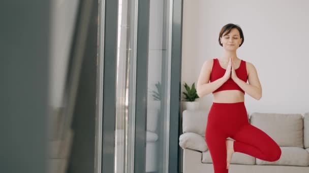 Mujer en un disfraz de fitness está haciendo ejercicio de yoga por la mañana en una estera — Vídeos de Stock