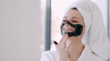Havluya sarılı saçları olan güzel bir kadın yüzüne siyah maske takıyor.