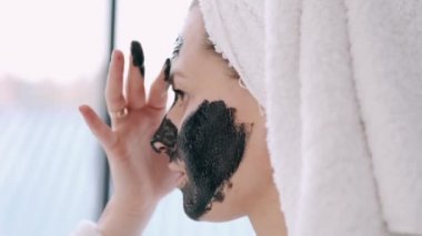 Havluya sarılı saçları olan güzel bir kadın yüzüne siyah maske takıyor.